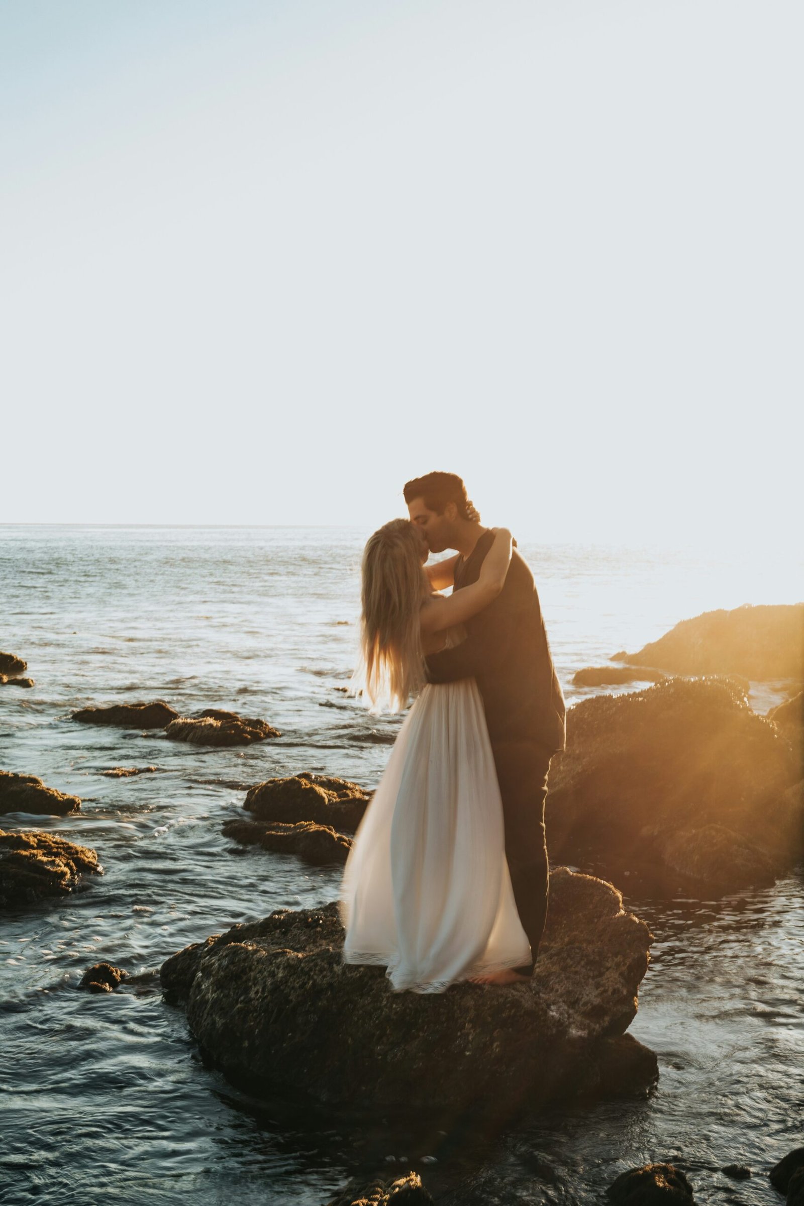 Wedding couple embracing on a rock by the Mediterranean Sea during their destination wedding in Barcelona, sharing an intimate and magical moment.